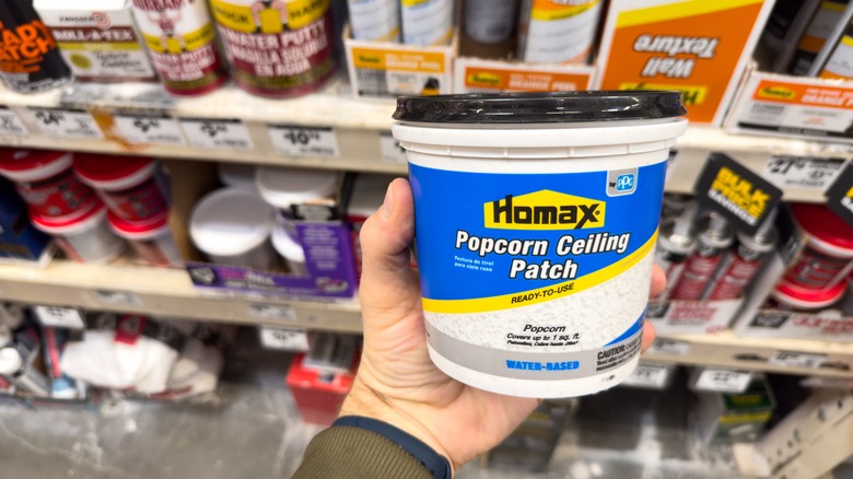A person holds a container of ready-to-use popcorn ceiling patch