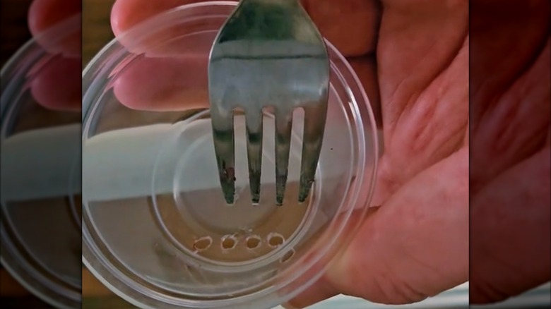 person piercing holes in the bottom of a clear cup with a hot fork