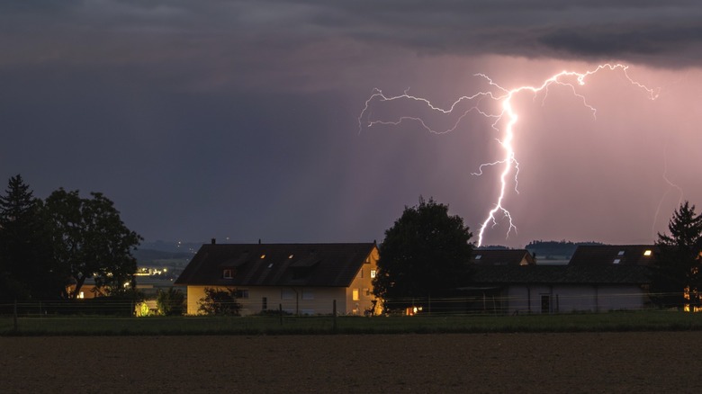 Purple and black sky with lightning striking near rural house