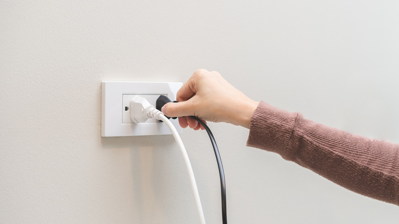 Person pulling TV plug from outlet before a thunderstorm