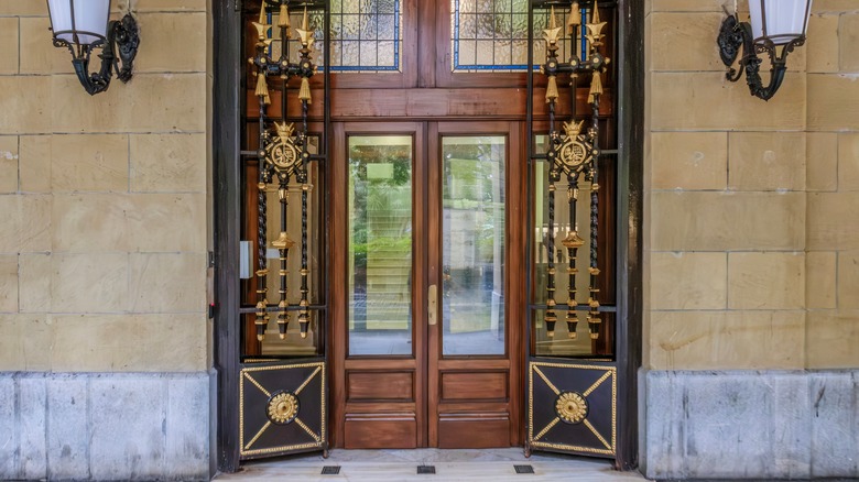Baroque styled grill gates open to a wooden front door.