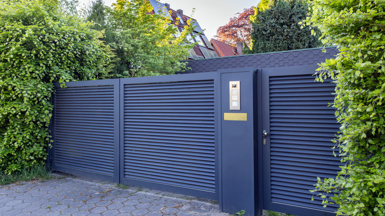 An austere horizontal rail grille gate that slides open in the front of a property.