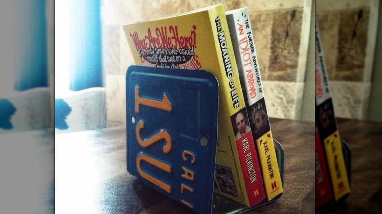 Blue California state license plate bent into a clever book holder, two paperbacks by Karl Pilkington inside