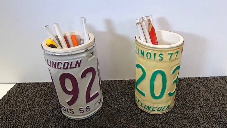 Two license plate pen cups each holding a set of pencils on a grey rubber mat