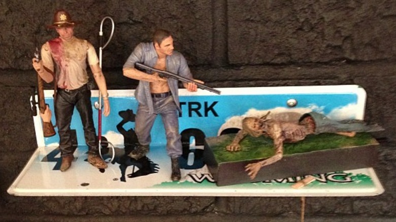 Walking Dead action figures displayed on a Wyoming license plate bent into a shelf