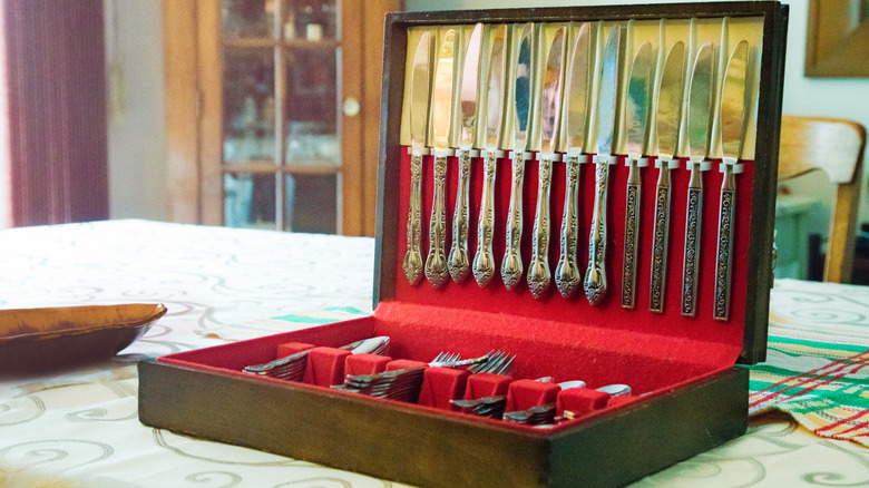An open vintage silverware box filled with silverware on a table with a a tablecloth