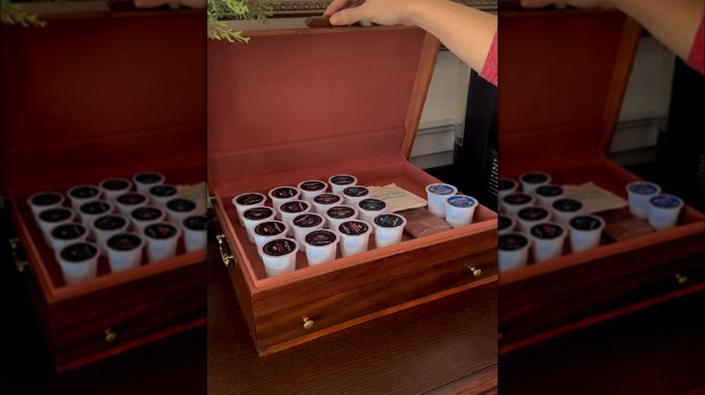 Person lifting top of silverware box to show interior full of k-cups, tea bags, and creamer pods