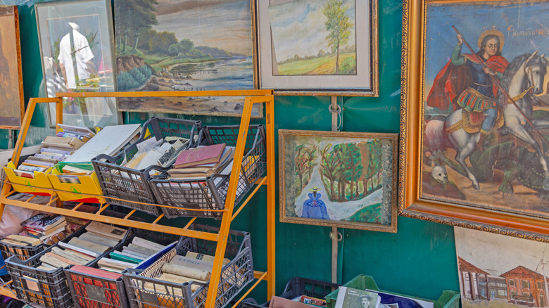 Various paintings and pieces of wall art are on display at a thrift store.