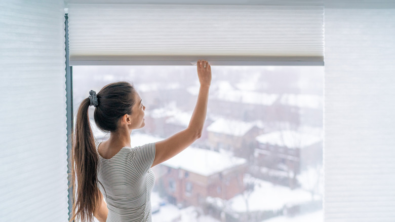 A woman closing cellular shades on an apartment's window