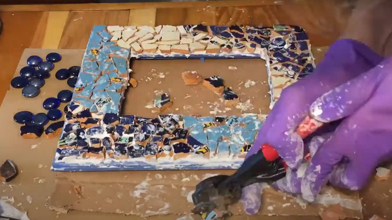 A pair of gloved hands putting together a mosaic frame