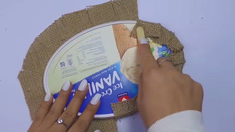 A pair of hands gluing a burlap around an ice cream lid.