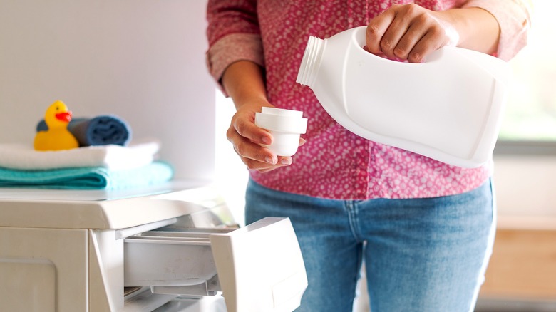 A person pours laundry detergent inside its cap