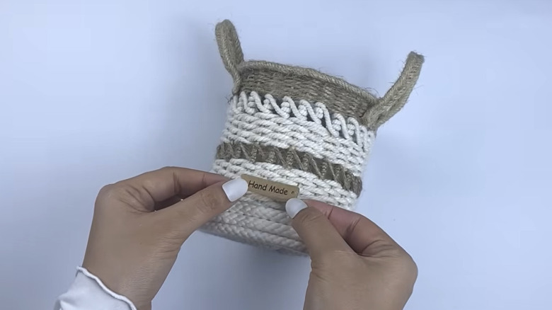 A woven basket made out of a coffee lid, bamboo skewers, and yarn in two colors.