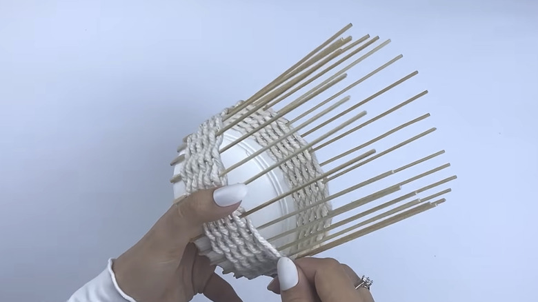 A person weaves yarn through some bamboo skewers.