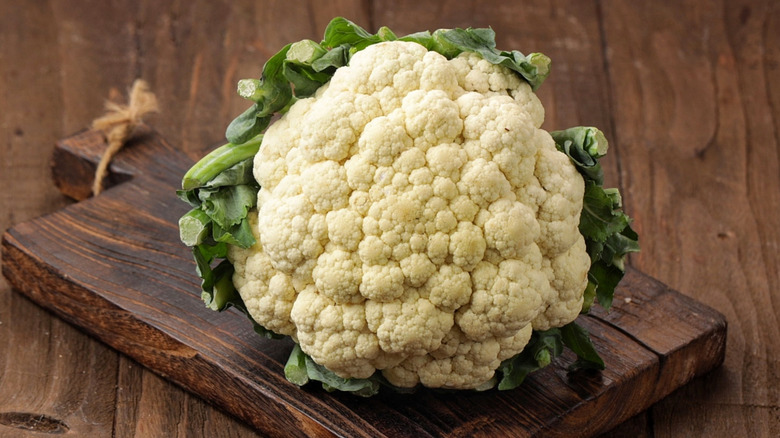 Cauliflower head sitting on a wood cutting board on a table