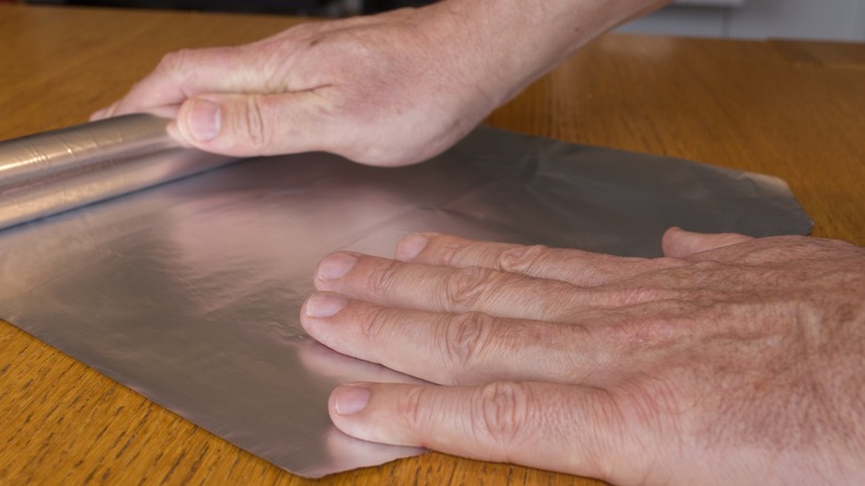 person rolling out aluminum foil