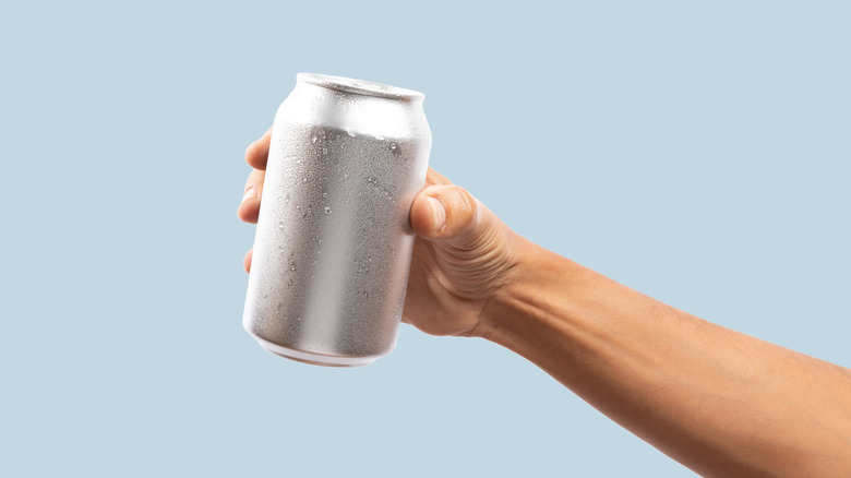 Hand holding cold silver aluminum can in his hand