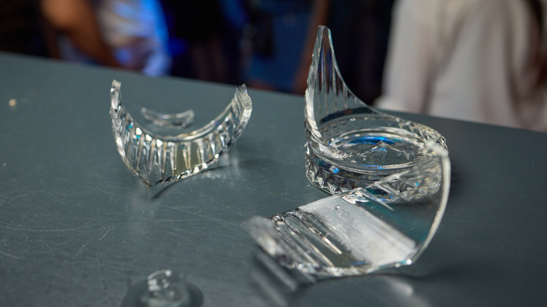A cut glass cocktail glass sits in pieces on a dark bar