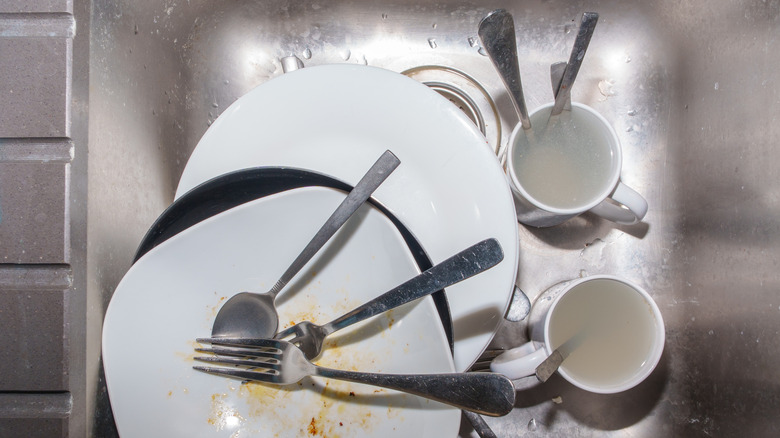 A pile of dirty dishes and silverware in the sink