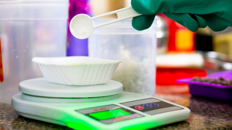 Close up of a gloved hand pouring lye into a container