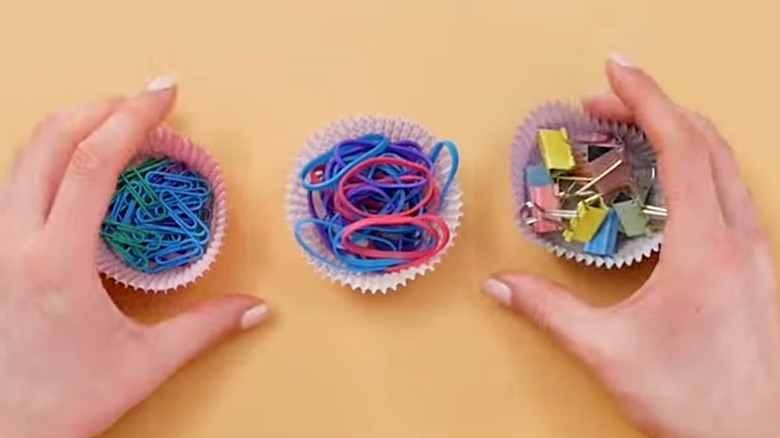 Hands wrapped around two cupcake liners filled with office supplies