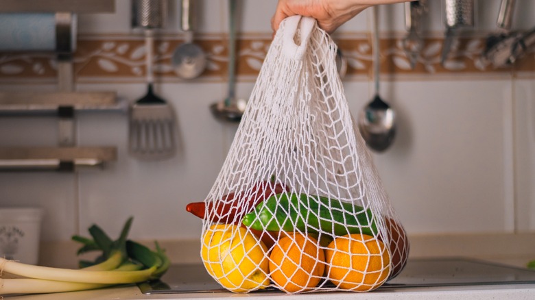 A mesh produce bag with oranges and peppers in it