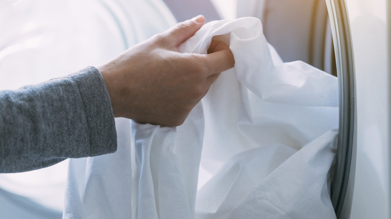 Hand pulling white sheet from dryer