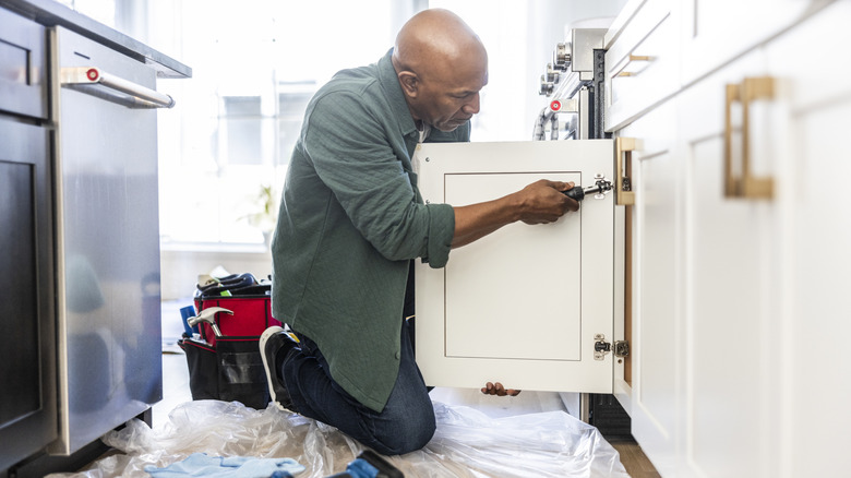 man unscrewing a cabinet door in a kitchen