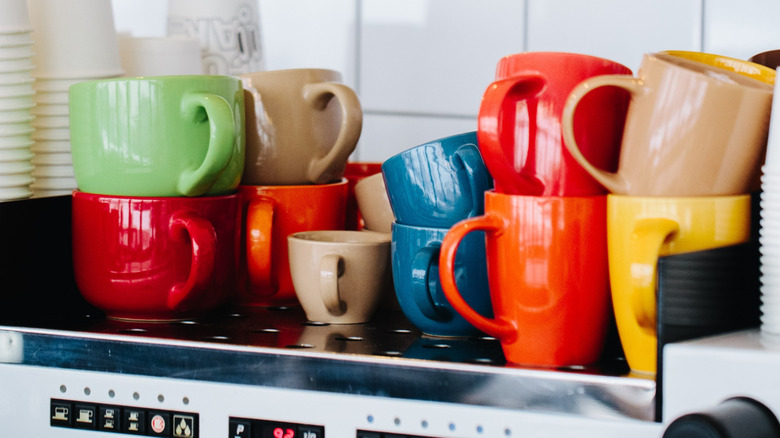 Colorful coffee mugs stacked haphazardly on a coffee machine