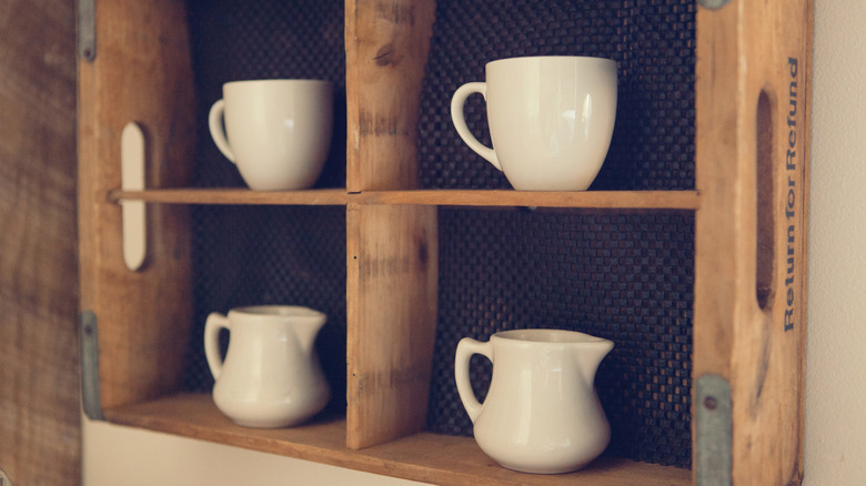 Old coffee mugs in a wooden crate on a wall