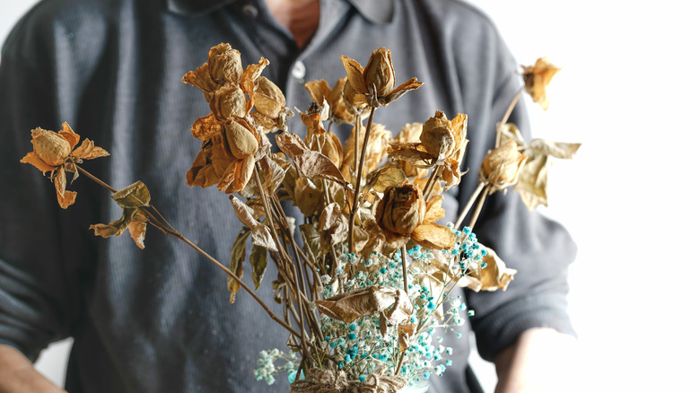 A man holding dead roses in a vase