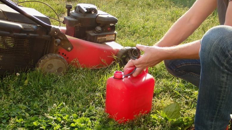 person opening red gas container next to lawn mower in lawn