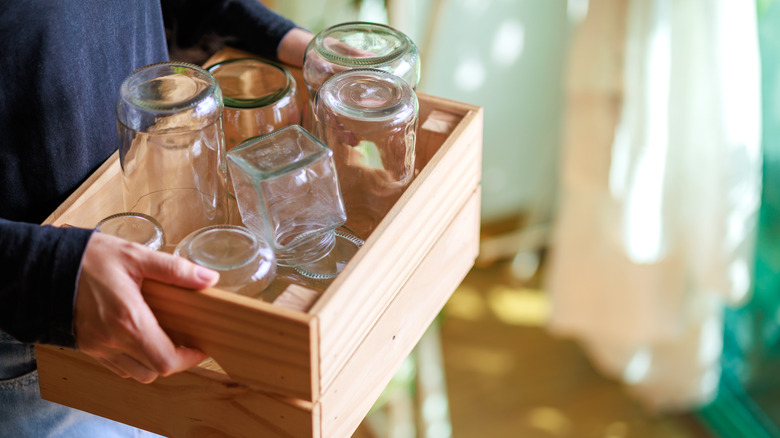 person holding a wooden crate full of empty glass jars