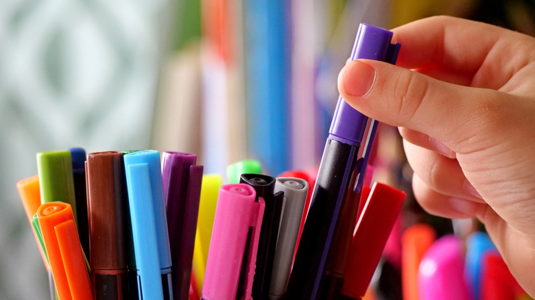 A hand selecting a purple marker from a collection of colorful choices.