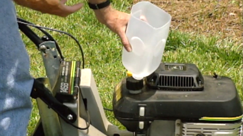 Man using milk bottle as funnel over fuel port in lawn equipment