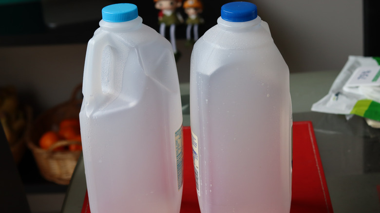 Two empty milk jugs with the top one, one in a lighter blue top and the other darker