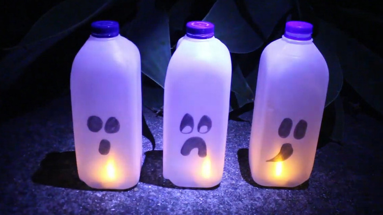 Three funny faced milk jug lanterns on concrete, each lit with a battery-operated tealight