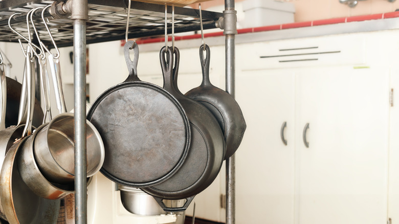 Old, scratched up, and dirty frypans hanging in a kitchen.