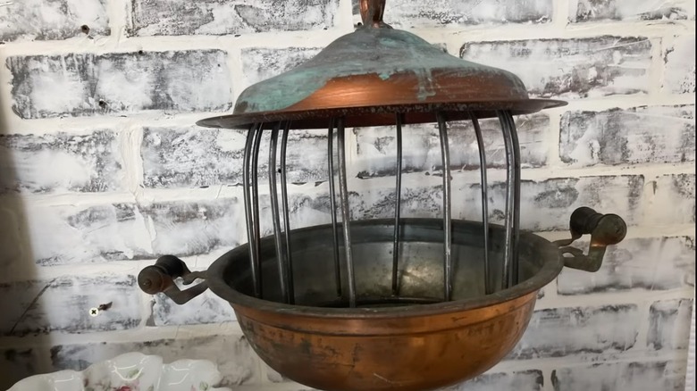 Metal bird bath against brick background.