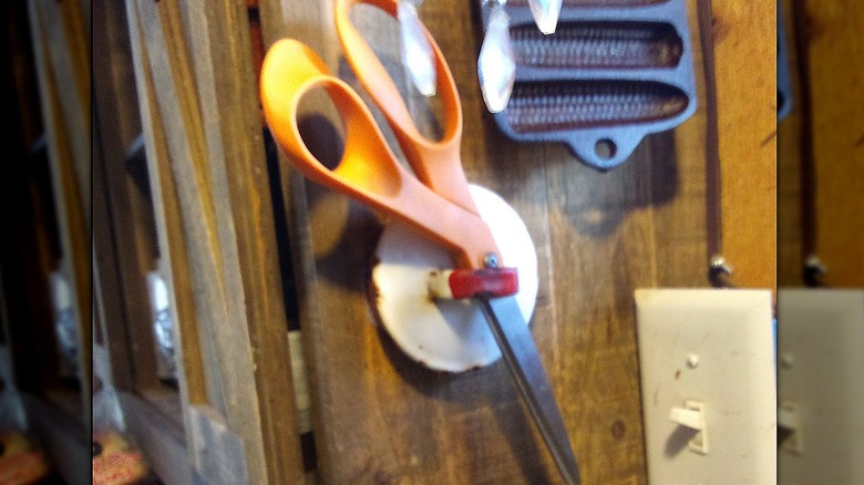 Orange scissors hanging on white and red lid.