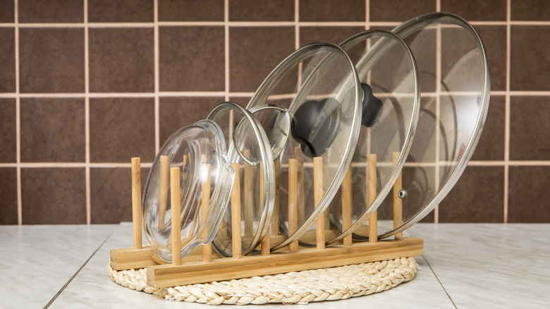 A wood rack holding glass pot and pan lids.