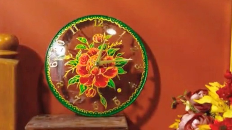 Glass red, green, and gold clock on wood surface.