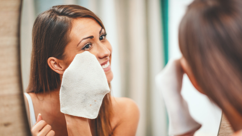 Woman wiping off face with a white washcloth