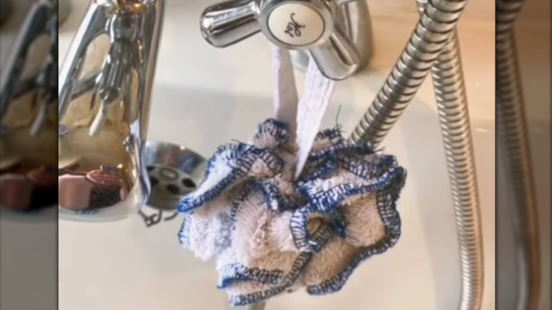 Handmade shower loofah made from a blue and white towel hangs from a faucet