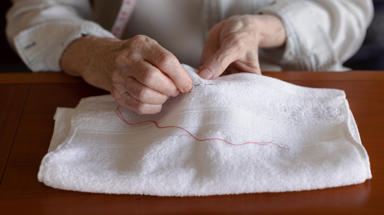 Hands sewing red thread into an old white towel