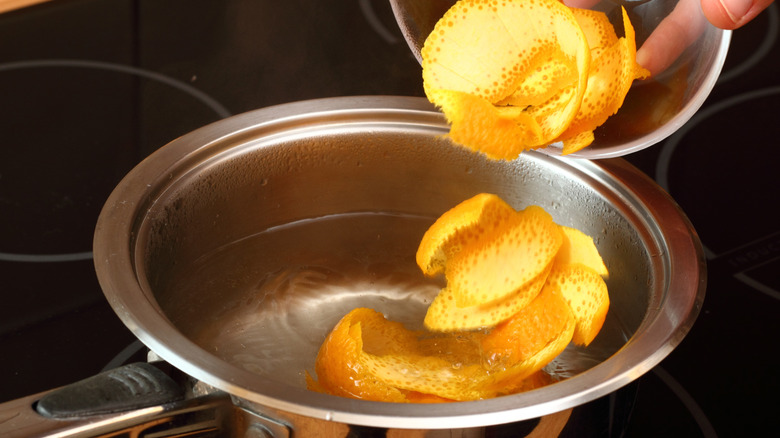 A lhand pours orange peels into a pot of boiling water.