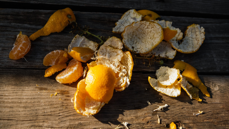 Orange peels and a few fruit slices sit on a wooden surface in sunlight.