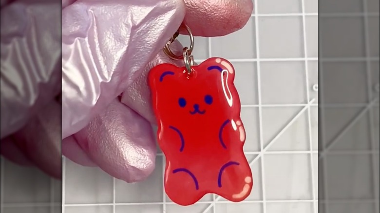 gloved hand holding a red teddy bear plastic keychain