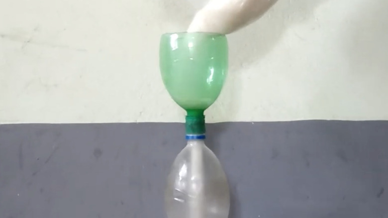 sugar pouring through green plastic bottle on top of other bottle, making a funnel