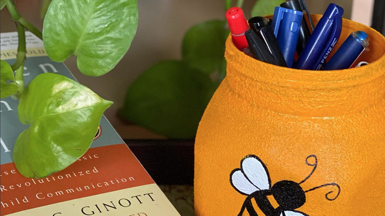 orange container with bee on it holding pens next to book